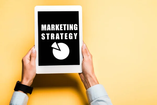 Cropped view of woman holding digital tablet with marketing strategy letters on orange — Stock Photo