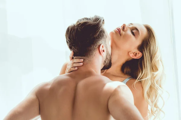 Вид сзади мужчина без рубашки целует чувственную подружку у окна дома — стоковое фото