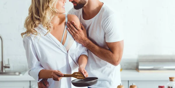 Cropped view of man hugging girlfriend preparing breakfast on frying pan — Stock Photo