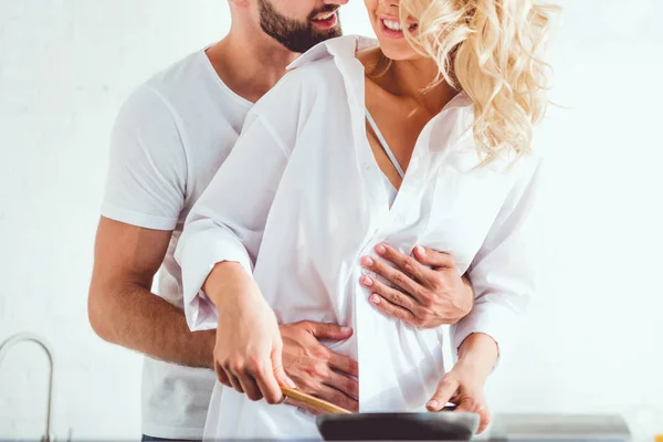 Cropped view of man hugging smiling girlfriend cooking breakfast on frying pan — Stock Photo