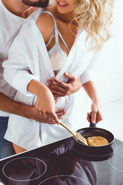 Vue recadrée de l'homme étreignant sourire petite amie cuisson crêpe sur poêle — Photo de stock
