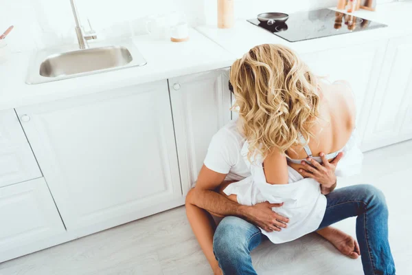 Vue grand angle de jeune couple étreignant assis sur le sol de la cuisine — Photo de stock