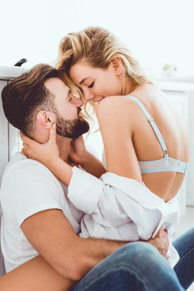 Cheerful young couple embracing while sitting on floor in kitchen — Stock Photo