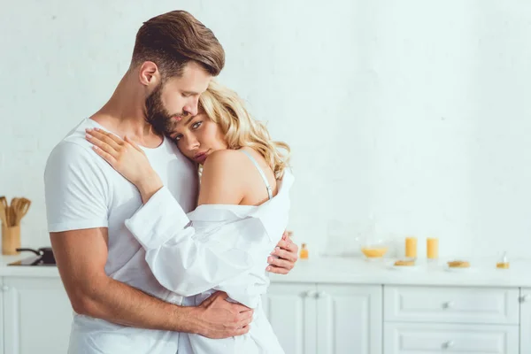 Beautiful young woman looking at camera while embracing with boyfriend in kitchen — Stock Photo