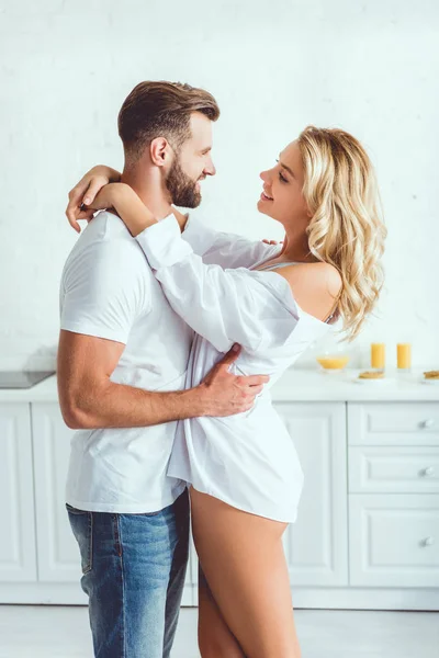 Feliz, bonito jovem abraçando sorridente namorada na cozinha — Fotografia de Stock