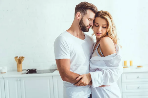 Glückliches junges Paar, das sich mit geschlossenen Augen in der Küche umarmt — Stockfoto