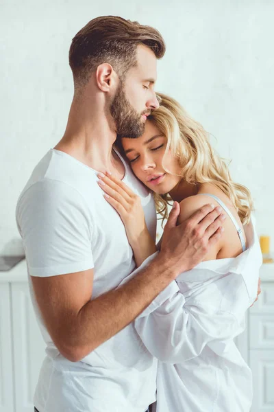 Guapo hombre abrazando joven hermosa novia en cocina - foto de stock