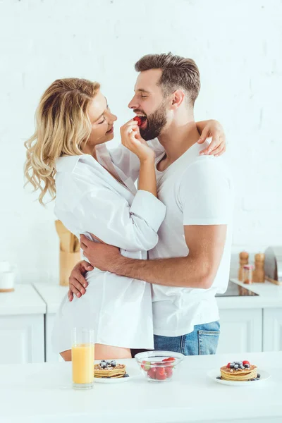 Young couple embracing while girlfriend feeding boyfriend with strawberry — Stock Photo