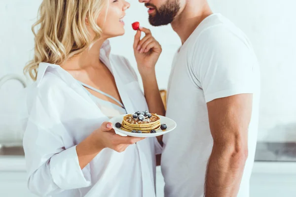 Cropped view of young woman holding plate with pancakes and strawberry near boyfriend — Stock Photo