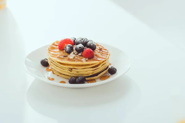 Plate of pancakes with blueberries and strawberries on white table — Stock Photo