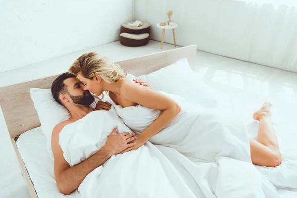 Young woman hugging and kissing boyfriend while lying in bed — Stock Photo