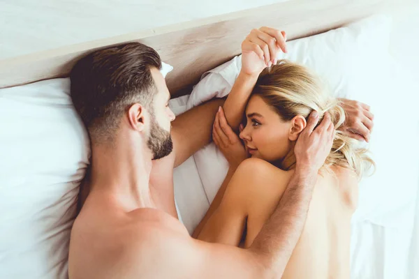 Young man hugging young, sexy girlfriend while lying in bed — Stock Photo