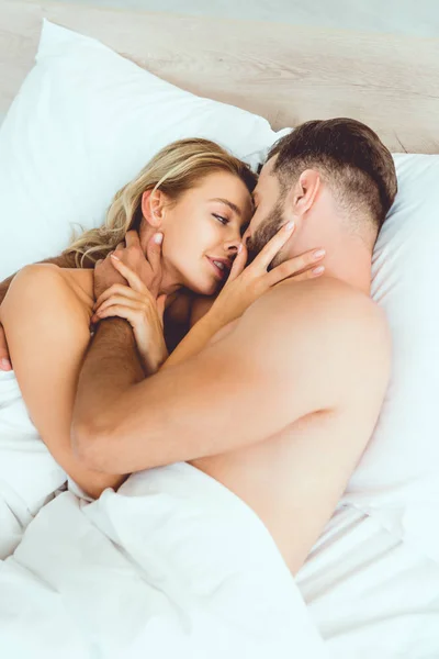 Feliz jovem casal abraçando e beijando enquanto deitado na cama — Fotografia de Stock