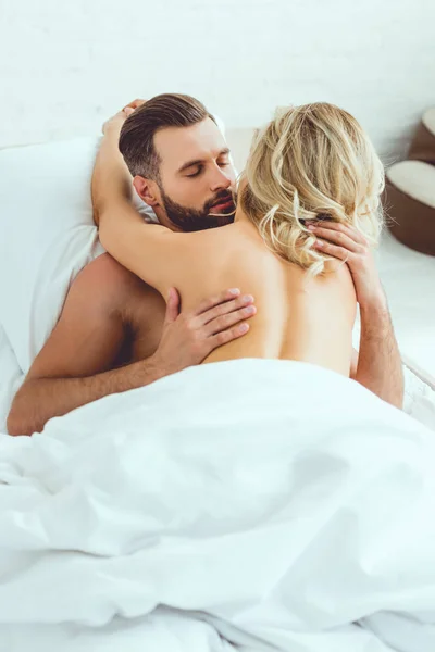 Vista posteriore di giovane donna abbracciando bel fidanzato mentre sdraiato a letto — Foto stock