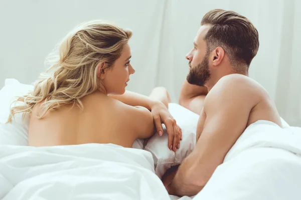 Beau jeune homme regardant loin tout couché dans le lit près de petite amie attrayante — Photo de stock