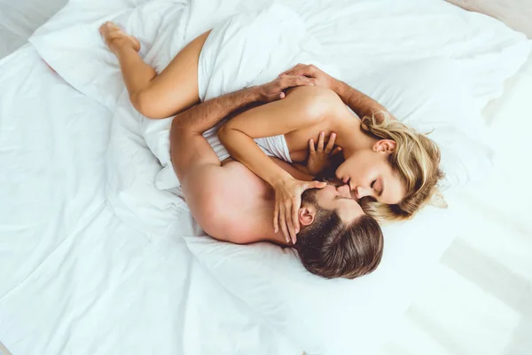 Top view of young couple embracing while lying on white bedding — Stock Photo