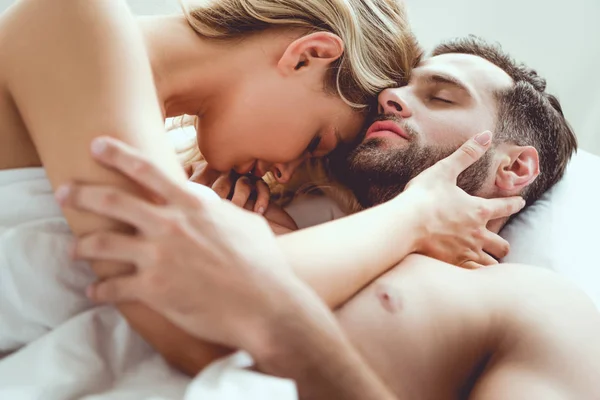 Feliz joven pareja abrazando con los ojos cerrados mientras está acostado en la cama - foto de stock