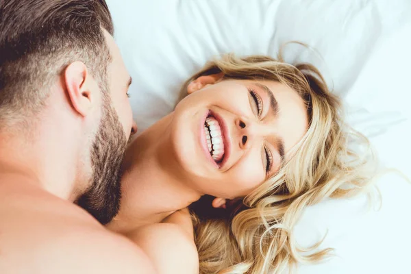 Cropped view of young man biting laughing girlfriend while lying in bed — Stock Photo