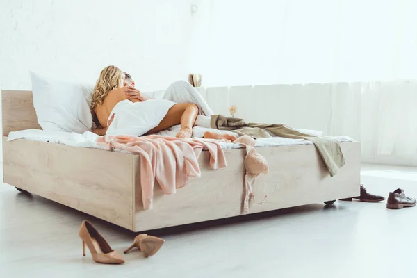 Jovem casal abraçando enquanto deitado em cama espaçosa perto de roupas — Fotografia de Stock