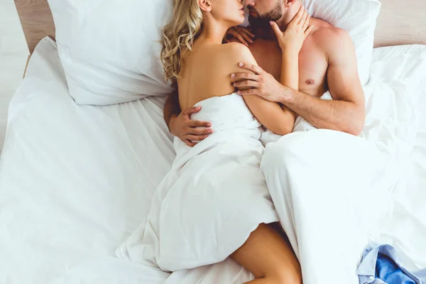 Обрізаний вид молодої пари, що обіймає і цілує, лежачи в ліжку — стокове фото