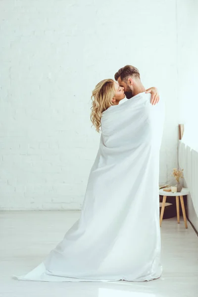 Happy young couple kissing while wrapping in white sheet — Stock Photo