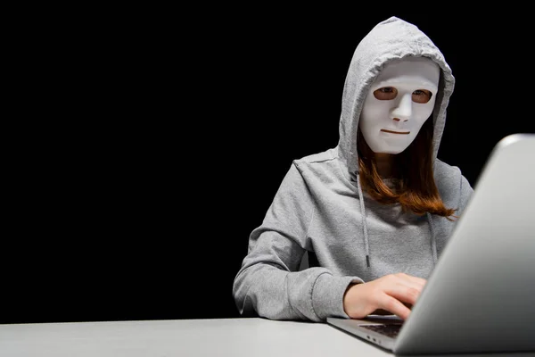 Anonymous internet troll in mask typing on laptop keyboard isolated on black — Stock Photo