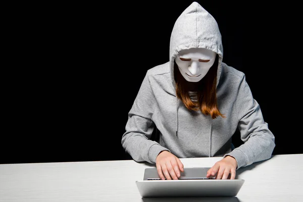 Anonymous internet troll in mask typing on laptop keyboard isolated on black — Stock Photo