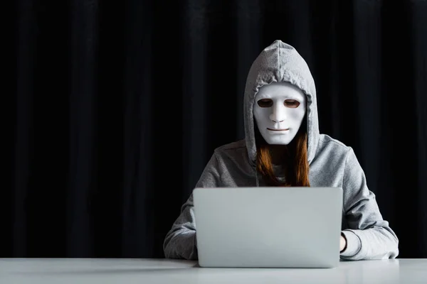 Anonymous internet troll in mask typing on laptop keyboard on black — Stock Photo