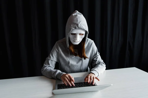 Troll de internet anônimo em máscara digitando no teclado do laptop em preto — Fotografia de Stock