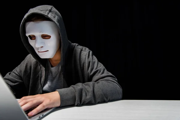 Troll internet anonyme en masque tapant sur clavier d'ordinateur portable isolé sur noir — Photo de stock