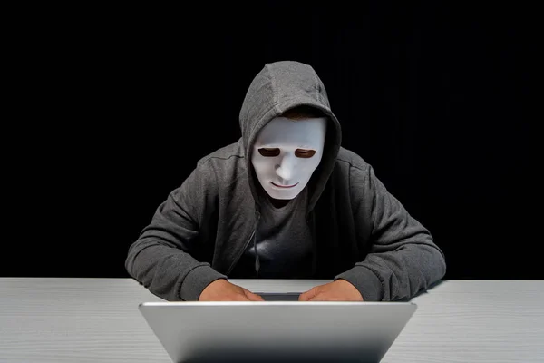 Anonymous internet troll in mask typing on laptop keyboard isolated on black — Stock Photo