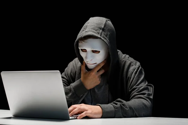 Anonymous internet troll in mask typing on laptop keyboard isolated on black — Stock Photo