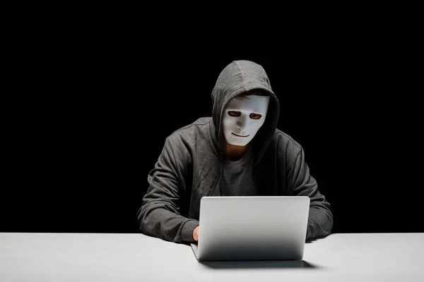 Анонимный интернет-тролль в маске, печатающий на клавиатуре ноутбука изолированный на черном — стоковое фото