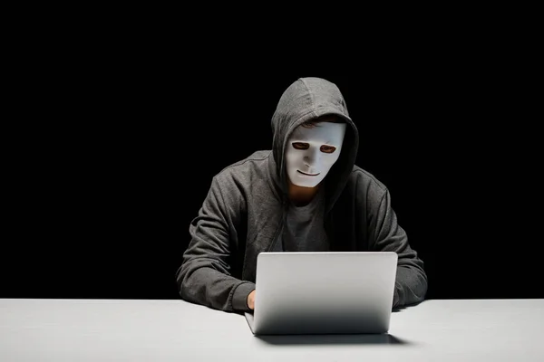 Anonymous internet troll in mask typing on laptop keyboard isolated on black — Stock Photo