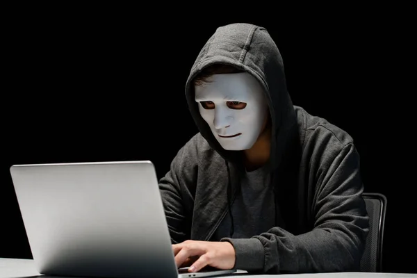 Anonymer Internet-Troll in Maske tippt auf Laptop-Tastatur isoliert auf schwarz — Stockfoto