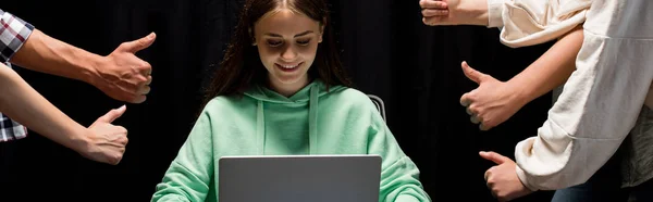 Panoramic shot of people showing thumbs up and smiling girl holding laptop on black — Stock Photo