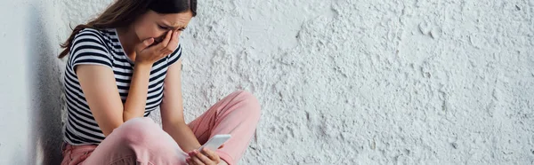 Panoramic shot of sad crying girl holding smartphone — Stock Photo