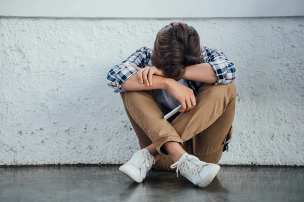 Triste adolescente sentado con las piernas cruzadas y la celebración de teléfono inteligente - foto de stock