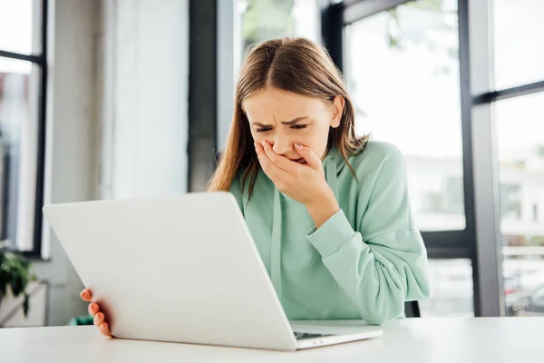 Chica triste en sudadera casual sentado en la mesa y el uso de la computadora portátil - foto de stock