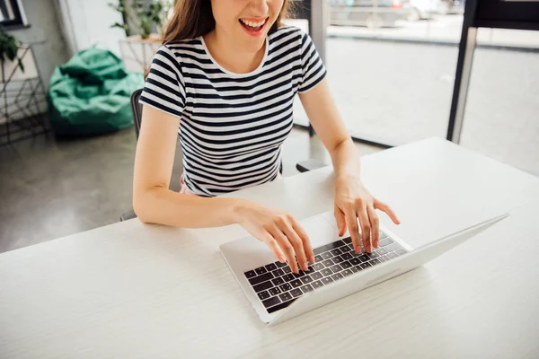 Vista parcial de la chica sonriente en camiseta a rayas usando el ordenador portátil en casa - foto de stock