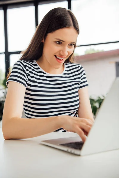 Smiling girl in striped t-shirt using laptop at home — Stock Photo