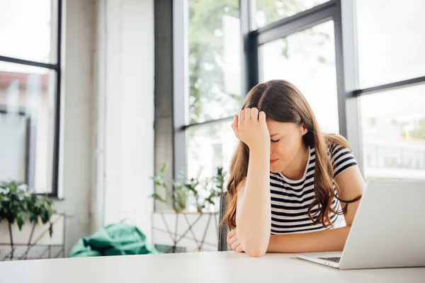 Chica triste en camiseta a rayas usando el ordenador portátil en casa - foto de stock