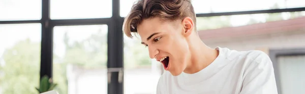 Panoramic shot of smiling teen boy in white t-shirt at home — Stock Photo