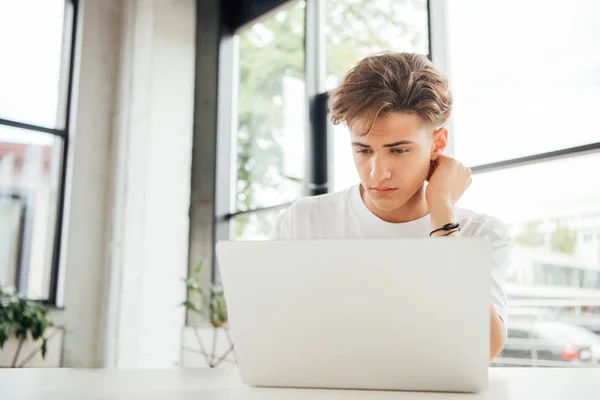 Pensive teen boy in white t-shirt using laptop at home — Stock Photo