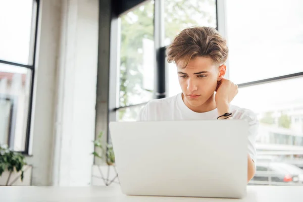 Pensoso teen boy in bianco t-shirt utilizzando il computer portatile a casa — Foto stock