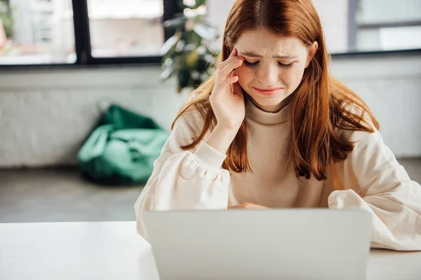 Sad teen girl sitting at table with laptop at home — Stock Photo