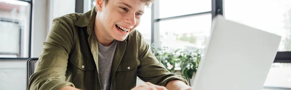 Tiro panorâmico de animado adolescente menino usando laptop em casa — Fotografia de Stock