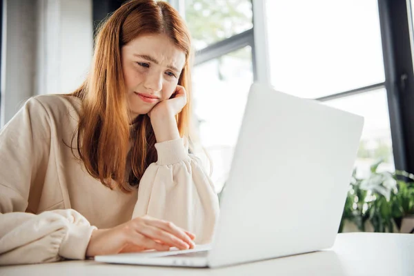 Sad teen girl sitting at table with laptop at home — Stock Photo