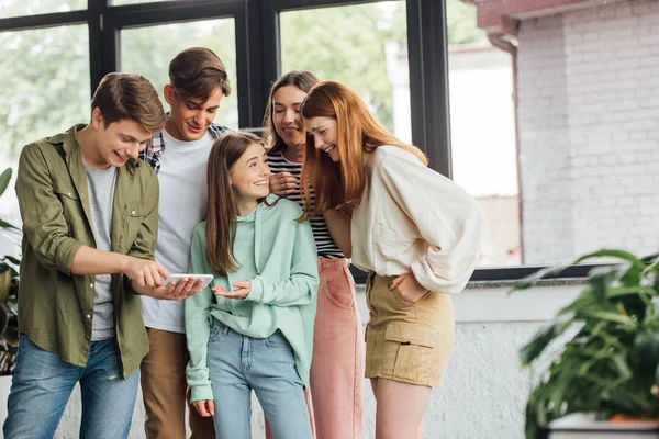 Group of happy friends laughing while using smartphone — Stock Photo