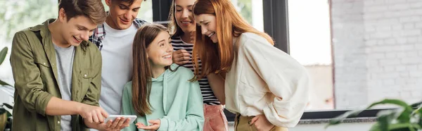 Panoramic shot of group of friends laughing while using smartphone — Stock Photo